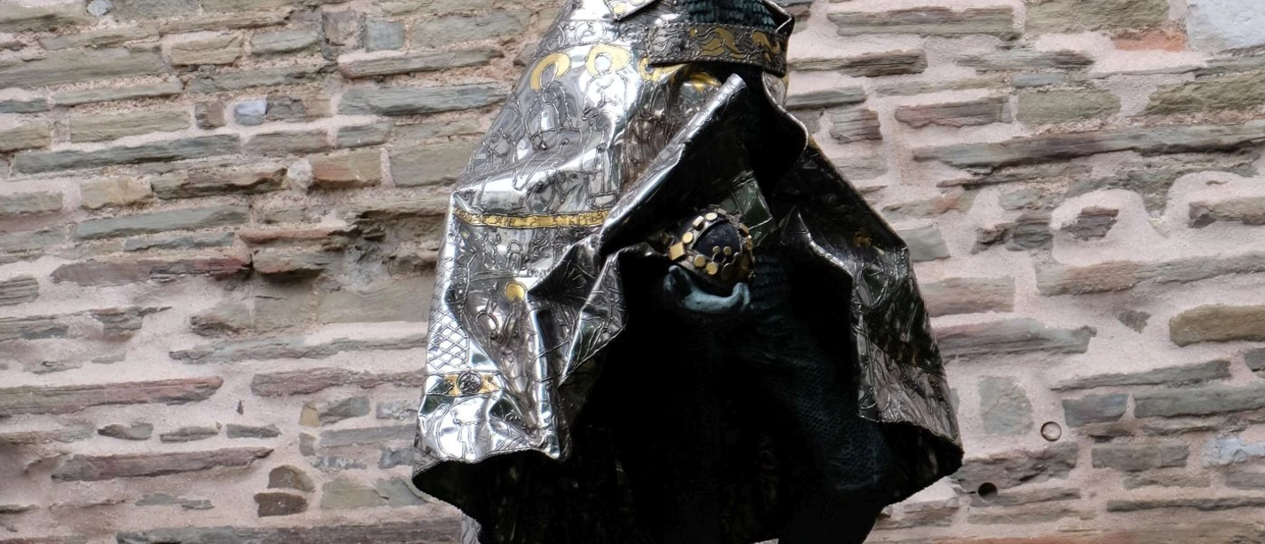 Die Bronzestatue zeigt einen gekrönten Mann im langen Umhang, vor einer Steinwand gehend.