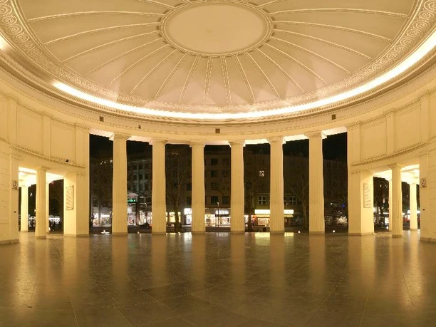 Rotunde des Elisenbrunnens mit mehreren Säulen und Innenbeleuchtung.