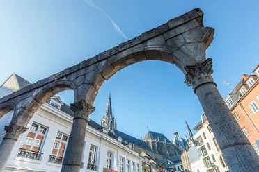 Römischer Portikus Steinerne Torbögen aus der Römerzeit stehen unter blauem Himmel im Hof. Im Hintergrund ragt der Aachener Dom empor.