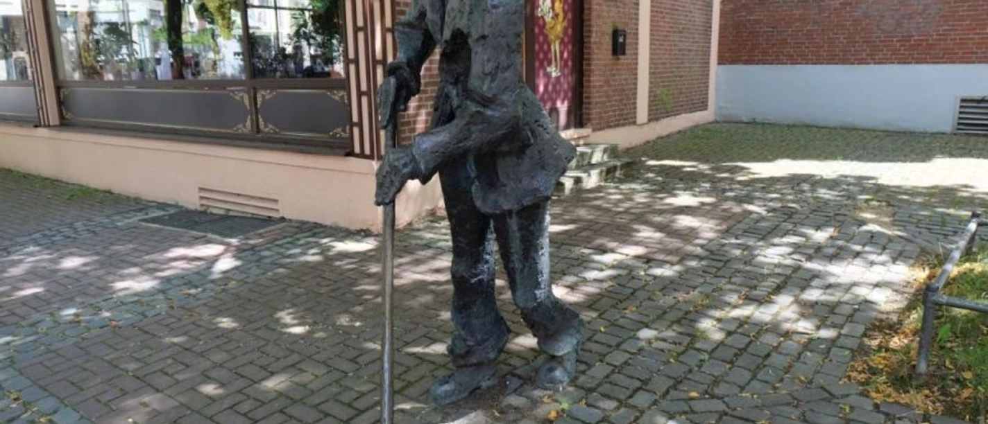 Eine Bronzeskulptur eines Straßenkehrers in Arbeitskleidung und mit Besen.