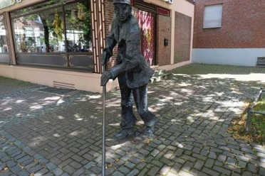 Kehrmännchen Eine Bronzeskulptur eines Straßenkehrers in Arbeitskleidung und mit Besen.