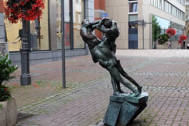 Bronzeskulptur von zwei Personen, die jeweils auf der Schulter eines anderen sitzen und miteinander kämpfen.