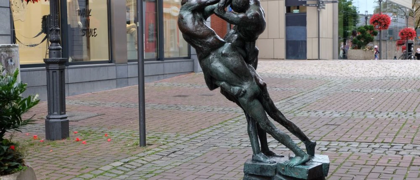 Bronzeskulptur von zwei Personen, die jeweils auf der Schulter eines anderen sitzen und miteinander kämpfen.