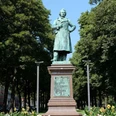 David-Hansemann-Denkmal Statue von einem Mann, der einen Arm in die Hüfte stützt, auf einem Sockel umgeben von Bäumen.