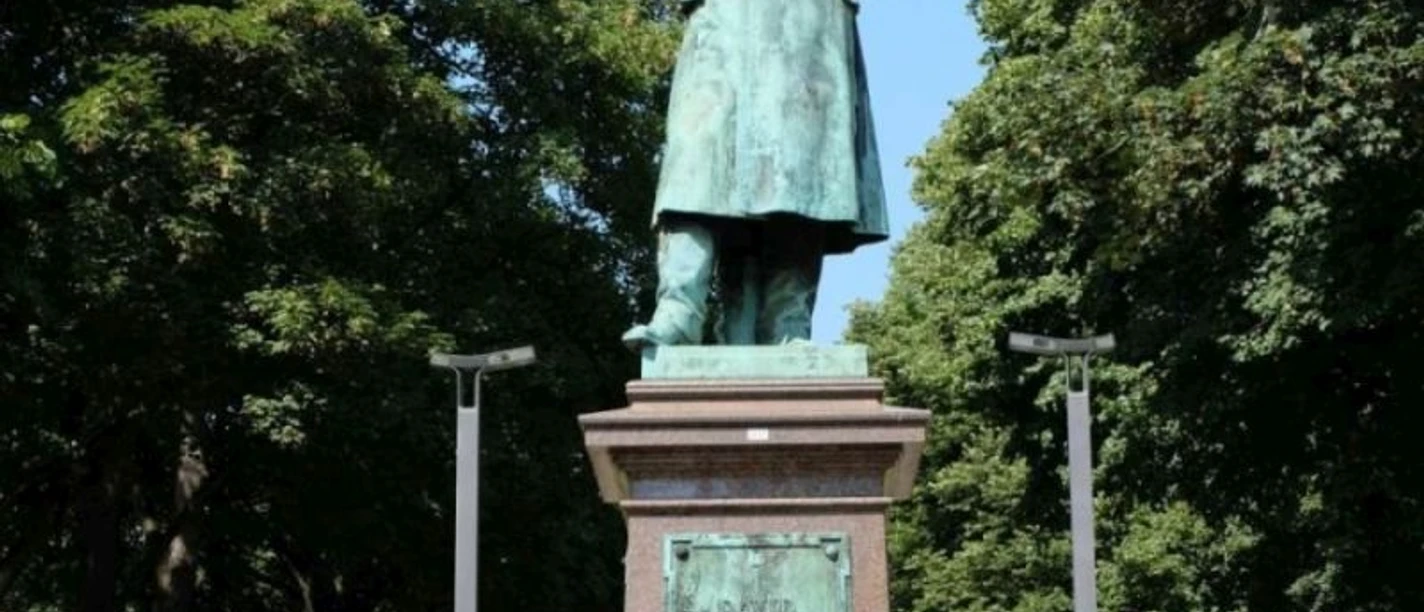 David-Hansemann-Denkmal Statue von einem Mann, der einen Arm in die Hüfte stützt, auf einem Sockel umgeben von Bäumen.