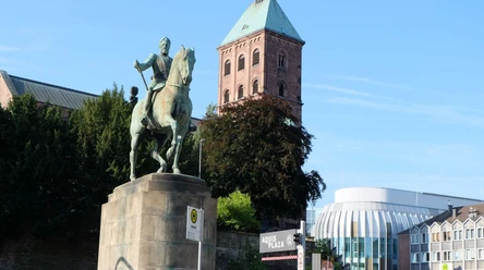 Auf einem steinernen Sockel steht das Denkmal von Kaiser Friedrich III auf einem Pferd. Im Hintergrund kann man das Dach des Einkaufszentrums Aquis Plaza erkennen.