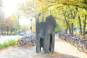 Eine Bronzeskulptur von vier Figuren im Gespräch, umgeben von Herbstlaub und Fahrrädern.