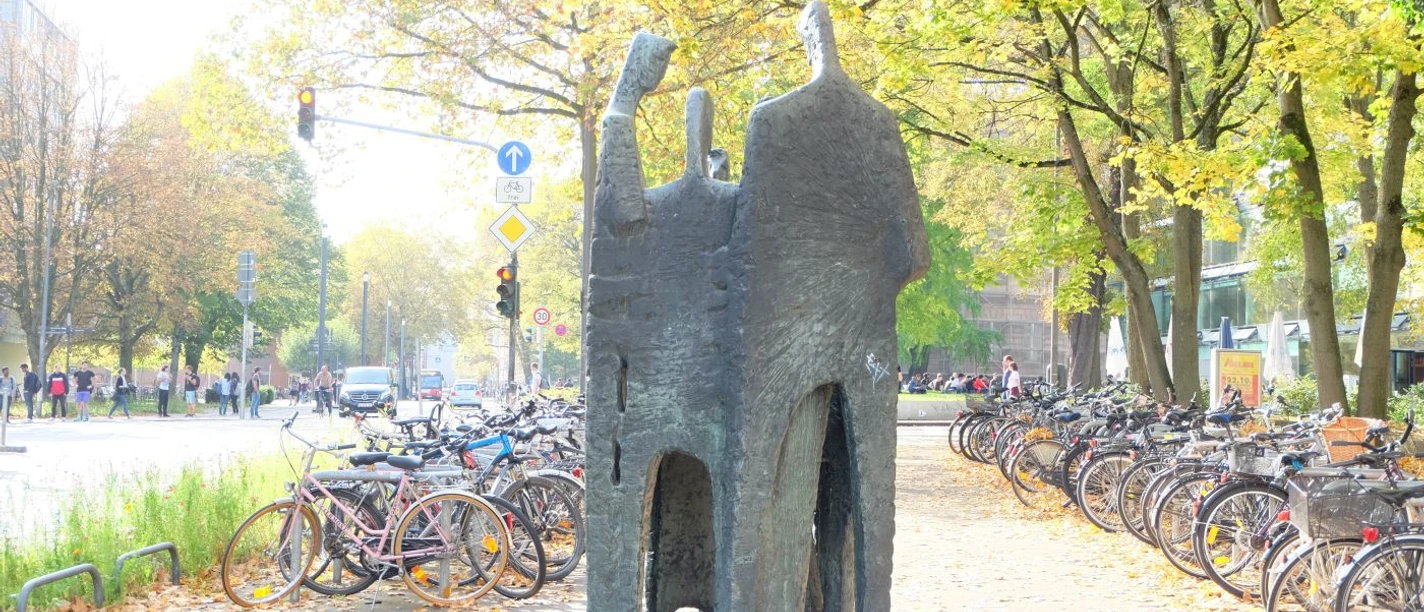 Menschen sprechen miteinander Eine Bronzeskulptur von vier Figuren im Gespräch, umgeben von Herbstlaub und Fahrrädern.