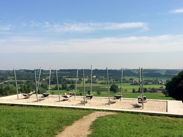 Lousberg Hängematten Acht Hängematten hängen auf einem erhöhten Plateau vor grünen Feldern unter klarem, blauem Himmel.