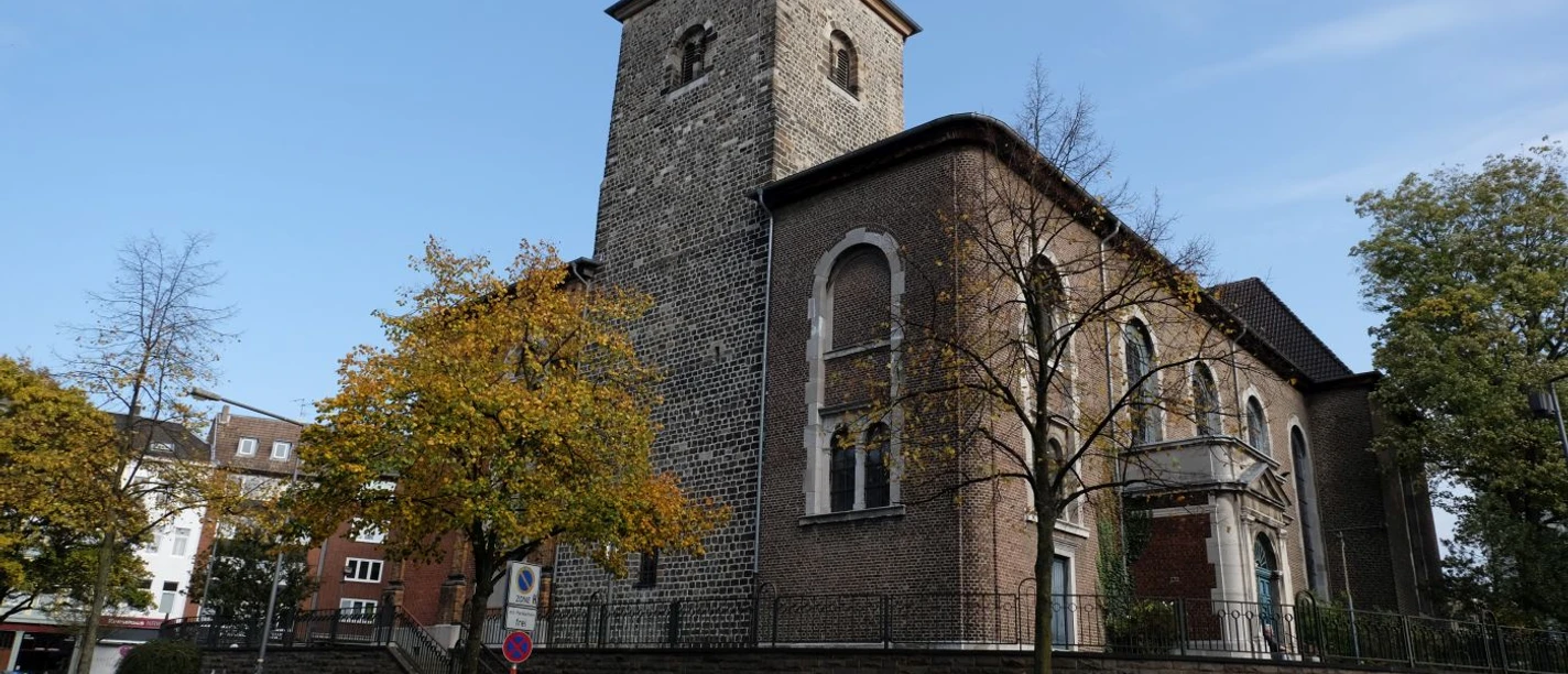 Kirche aus Stein, umgeben von Bäumen, unter einem klaren blauen Himmel.