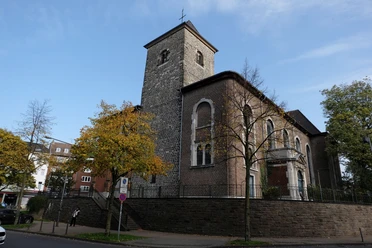 St. Peter Kirche aus Stein, umgeben von Bäumen, unter einem klaren blauen Himmel.