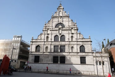 Kirche an der Jesuitenstraße mit heller, geschwungener Fassade und filigranen Verzierungen vor einem strahlend blauen Himmel.