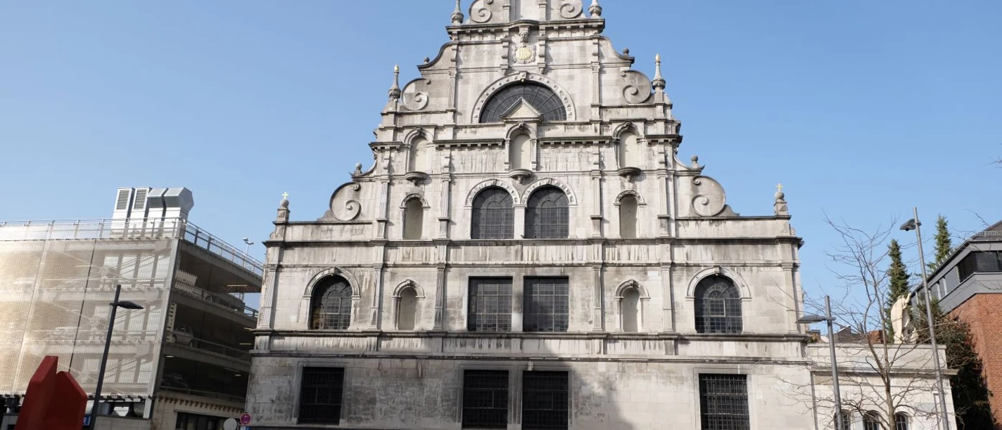 Kirche an der Jesuitenstraße mit heller, geschwungener Fassade und filigranen Verzierungen vor einem strahlend blauen Himmel.