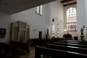Innenansicht der Klosterkirche mit schlichter Einrichtung, Kirchenbänken und bunten Glasfenstern.