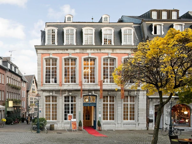 Das Couven-Museum, auf der Ecke eines gepflasterten Platzes, mit hellem rotem Anstrich, großen Sprossenfenstern und einem roten Teppich am Eingang.