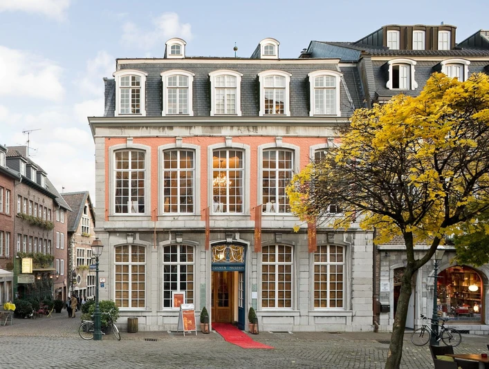Couven Museum Das Couven-Museum, auf der Ecke eines gepflasterten Platzes, mit hellem rotem Anstrich, großen Sprossenfenstern und einem roten Teppich am Eingang.