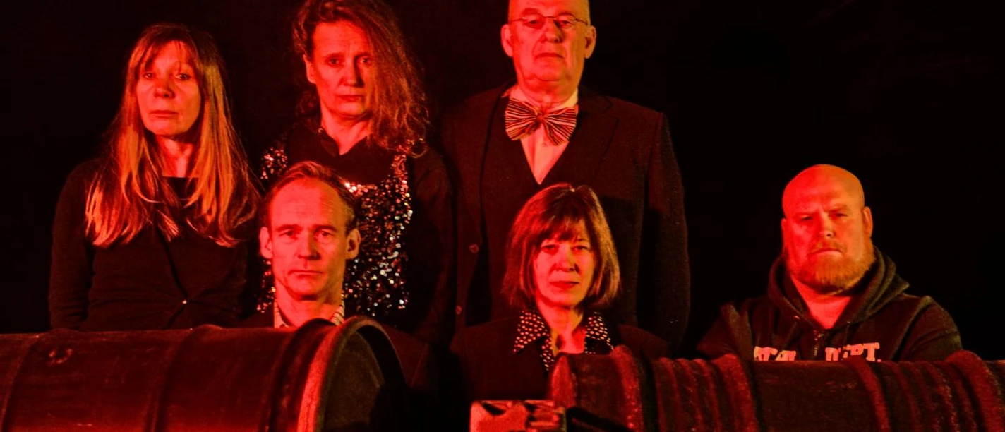 Theater K Sechs Personen, teils stehend, teils sitzend, werden von rotem Licht angeleuchtet und schauen in die Kamera.