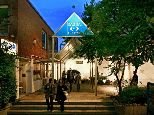 Eingangsbereich mit beleuchtetem Schild des DAS DA Theaters und Überdachung.