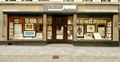 Mehrere Kunstwerke hinter großen Schaufenstern in dekorativen Rahmen. Der Eingang befindet sich im Zentrum des Bildes. Ein großes Firmenschild hängt oberhalb der Ausstellungsfläche.
