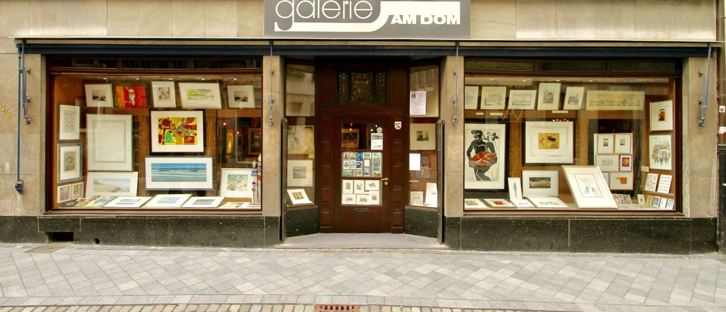 Galerie am Dom Mehrere Kunstwerke hinter großen Schaufenstern in dekorativen Rahmen. Der Eingang befindet sich im Zentrum des Bildes. Ein großes Firmenschild hängt oberhalb der Ausstellungsfläche.