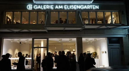 Abendlich beleuchtete Galeriefront mit Menschen vor der "Galerie am Elisengarten".