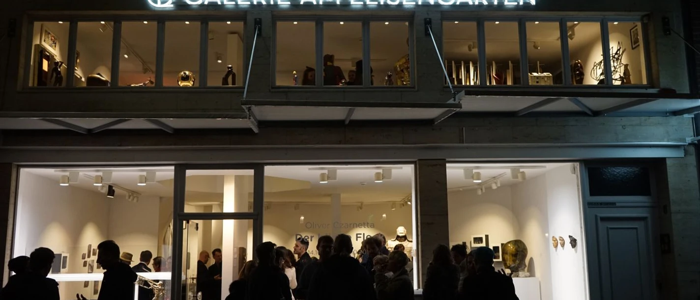 Abendlich beleuchtete Galeriefront mit Menschen vor der "Galerie am Elisengarten".