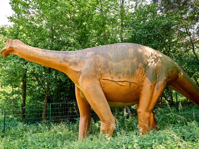 Modell eines Megalosauriers an den Saurierfährten in Bad Essen – Barkhausen. Lebensgroße Dinosaurierfigur in einem von Bäumen umgebenen Grünstreifen.
