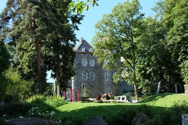 Frankenberger-Park Altes Bruchsteinhaus hinter einem Spielplatz inmitten eines Parks mit Bäumen und Wiesen.