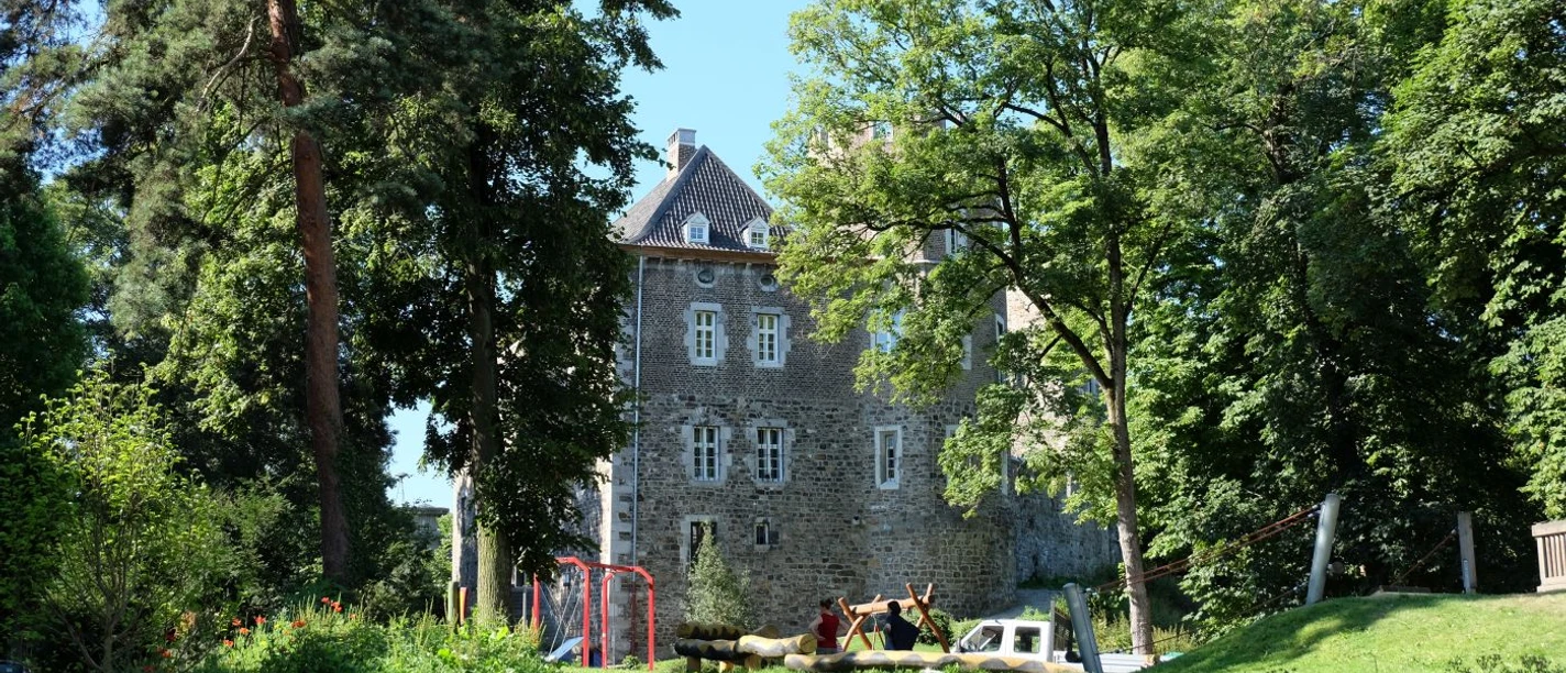 Frankenberger-Park Altes Bruchsteinhaus hinter einem Spielplatz inmitten eines Parks mit Bäumen und Wiesen.