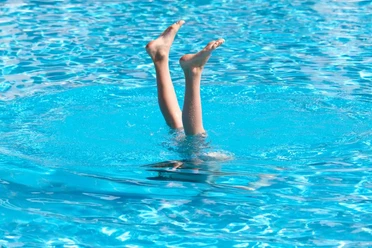Osthalle Zwei Beine ragen aus dem Wasser eines türkisen Schwimmbeckens.