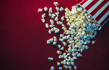 Ein umgefallener Popcornbecher mit rot-weißen Streifen, Popcorn verteilt sich auf rotem Hintergrund.