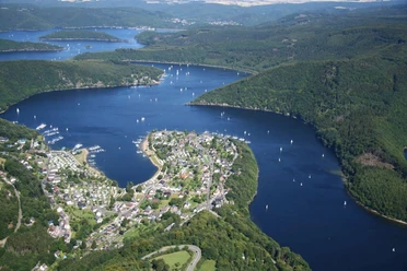 Rursee Panoramaansicht des sich schlängelnden Rursees mit grünen Hügeln und Segelbooten unter blauem Himmel.