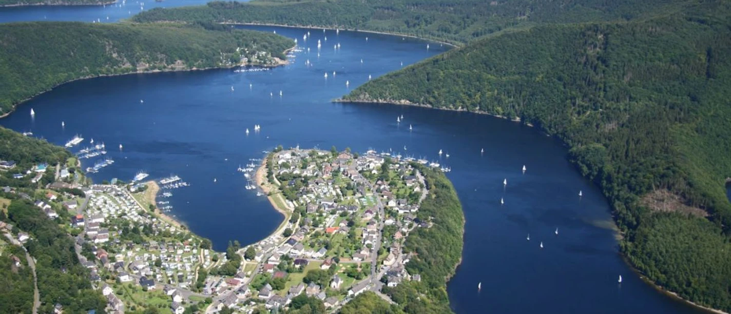 Rursee Panoramaansicht des sich schlängelnden Rursees mit grünen Hügeln und Segelbooten unter blauem Himmel.