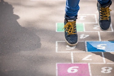 Spielplatz Wiesental Ein Kind in blauer Jeans und schwarzen Sneakers spielt auf einer mit Zahlen bemalten Straße ein Hüpfspiel..