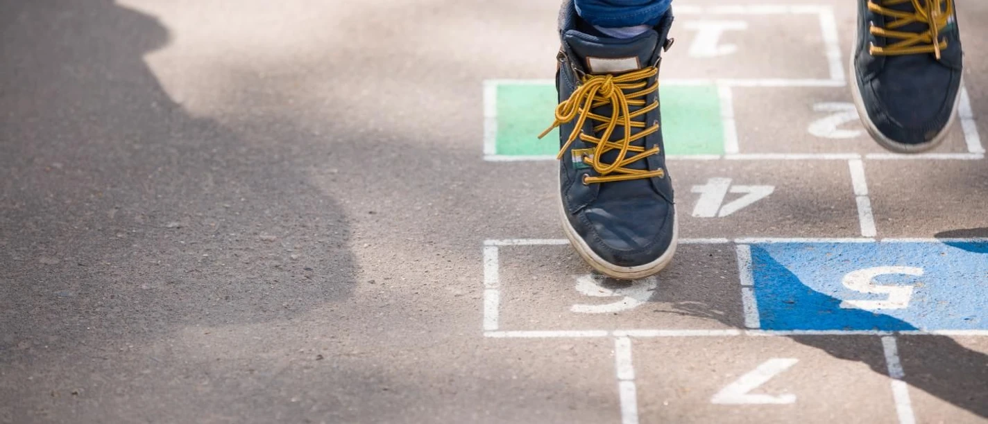 Spielplatz Wiesental Ein Kind in blauer Jeans und schwarzen Sneakers spielt auf einer mit Zahlen bemalten Straße ein Hüpfspiel..
