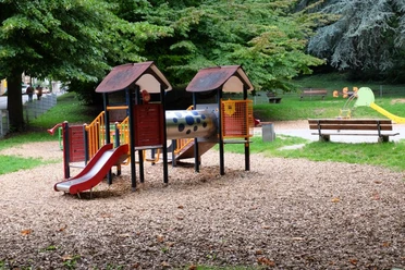 Spielplatz Veltmanplatz (c) ats Spielplatz auf Holzspänen mit einem bunten Klettergerüst, einer Rutsche und mehreren Holzbänken.