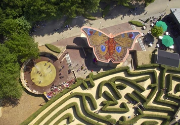 Blick von oben auf ein Labyrinth und ein Gebäude, dessen Dach einen bunten Schmetterling formt.