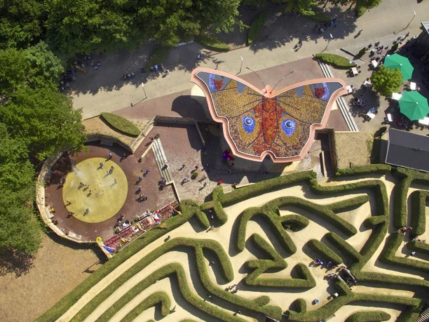 Blick von oben auf ein Labyrinth und ein Gebäude, dessen Dach einen bunten Schmetterling formt.