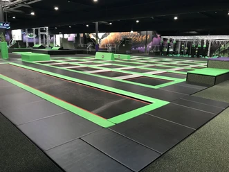 SuperFly Indoor-Trampolin-Halle mit in den Boden eingelassenen Trampolinnetzen, die mit grünen Schutzrändern umrandet sind.