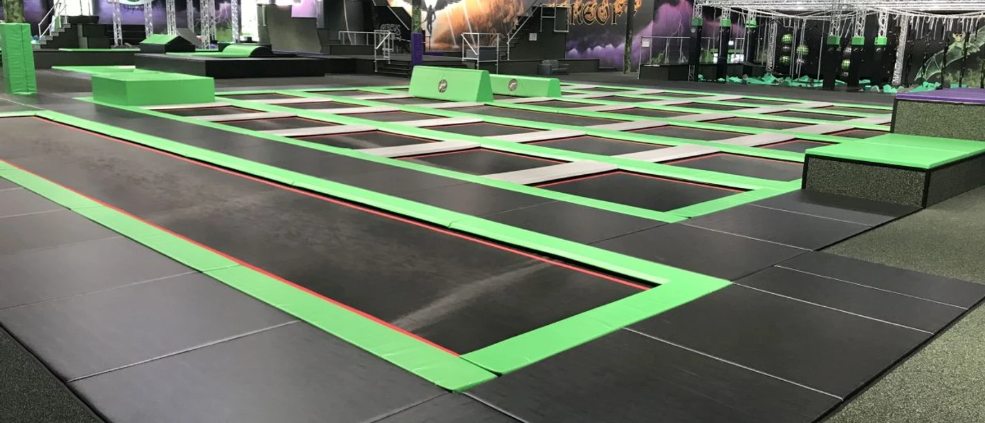 SuperFly Indoor-Trampolin-Halle mit in den Boden eingelassenen Trampolinnetzen, die mit grünen Schutzrändern umrandet sind.