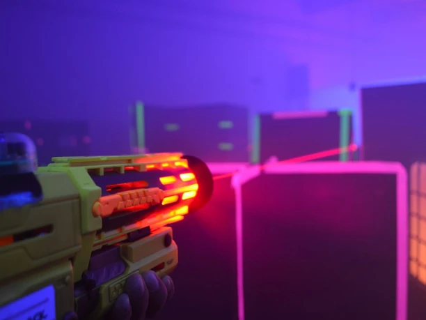Black LaserTag Aachen Eine Person hält eine leuchtende Lasertag-Pistole in einem abgedunkelten Raum, während farbige Laserstrahlen durch den Raum schießen.