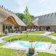 Außenbereich eines ländlichen Wellnesshotels mit Reetdach, Pool und Liegestühlen.Outdoor area of a rural wellness hotel with thatched roof, pool and sun loungers.Udendørs område på et landligt wellness-hotel med stråtag, pool og liggestole.Buitenruimte van een landelijk wellnesshotel met rieten dak, zwembad en ligstoelen.