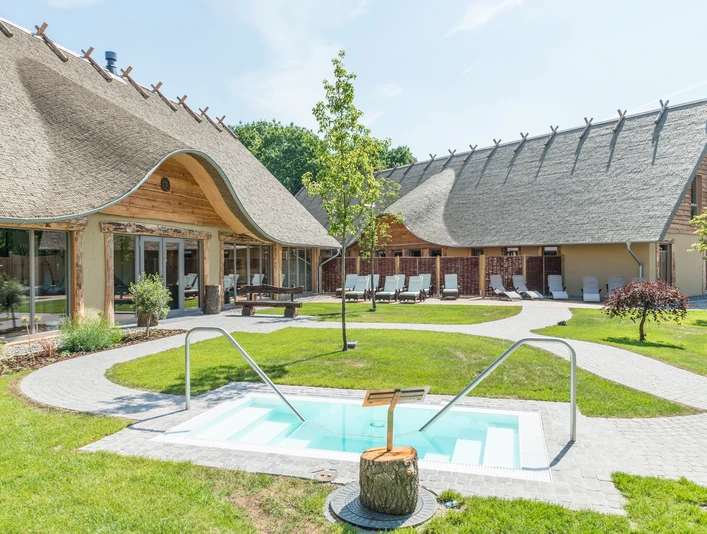Außenbereich eines ländlichen Wellnesshotels mit Reetdach, Pool und Liegestühlen.Outdoor area of a rural wellness hotel with thatched roof, pool and sun loungers.Udendørs område på et landligt wellness-hotel med stråtag, pool og liggestole.Buitenruimte van een landelijk wellnesshotel met rieten dak, zwembad en ligstoelen.