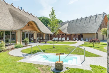 Im Stil der Germanen: Das Alfen Saunaland Außenbereich eines ländlichen Wellnesshotels mit Reetdach, Pool und Liegestühlen.