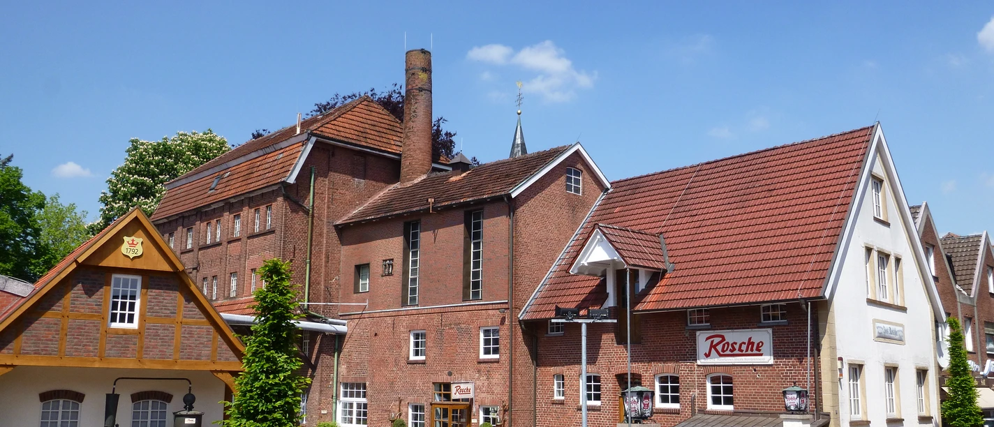Edelkornbrennerei Jos. Rosche Edelkornbrennerei mit rotem Ziegeldach, Schornstein und Innenhof bei blauem Himmel in Haselünne.