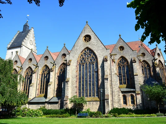 De Griese Toarn en de parochiekerk Mariae Geburt zijn bezienswaardigheden in Bad Laer in het Osnabrücker LandGotische Backsteinkirche mit großen Buntglasfenstern und grünem Garten im Vordergrund.