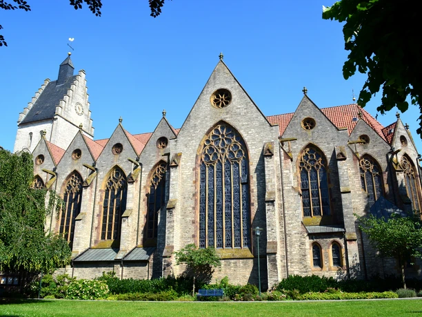 De Griese Toarn en de parochiekerk Mariae Geburt zijn bezienswaardigheden in Bad Laer in het Osnabrücker LandGotische Backsteinkirche mit großen Buntglasfenstern und grünem Garten im Vordergrund.