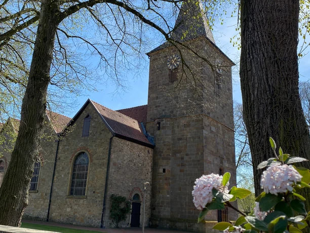 Ehemalige Kirche Hagen aTW Alte Steinkirche mit Turm und blühenden Zweigen im Vordergrund an einem sonnigen Tag.