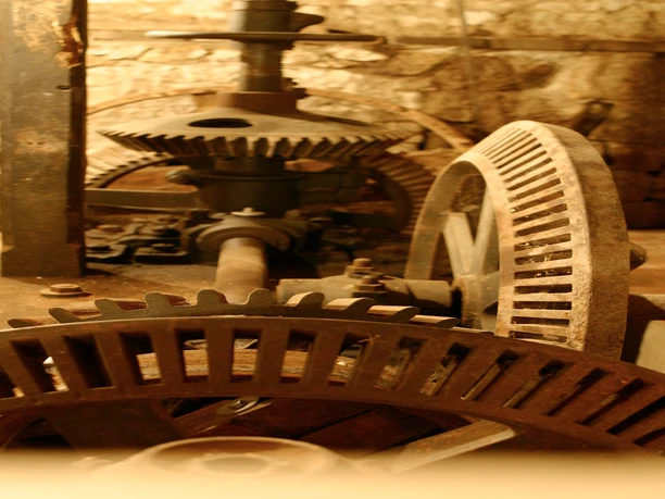 Gellenbecker-Muehle-Muehlrad_CC_Gemeinde-Hagen aTW Rostige Zahnräder einer historischen Maschine in einem erdigen, schummrigen Raum.