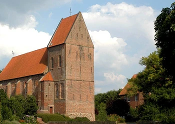 Gedächniskirche Rhede Backsteinkirche mit hohem Turm und rotem Ziegeldach, umgeben von Bäumen und blauem Himmel.
